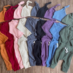 Peut inclure: Un ensemble de 10 tenues pour b&eacute;b&eacute; dans diff&eacute;rentes couleurs, notamment orange, rouge, rose, beige, gris, noir, violet, bleu et vert. Chaque tenue comprend un haut &agrave; manches longues et un pantalon assorti avec une taille &agrave; cordon. Les tenues sont en tissu gaufr&eacute; doux. Chaque tenue comprend &eacute;galement un bonnet gaufr&eacute; assorti avec un n&oelig;ud sur le dessus.