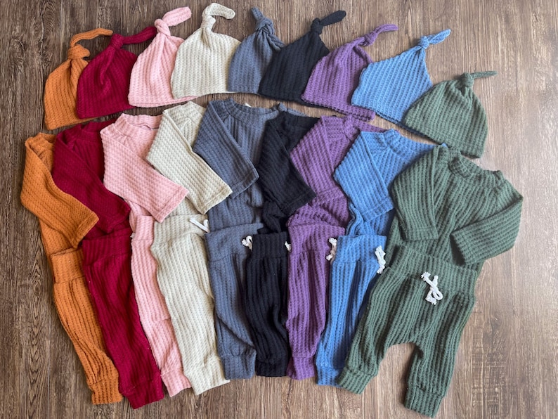 Peut inclure: Un ensemble de 10 tenues pour b&eacute;b&eacute; dans diff&eacute;rentes couleurs, notamment orange, rouge, rose, beige, gris, noir, violet, bleu et vert. Chaque tenue comprend un haut &agrave; manches longues et un pantalon assorti avec une taille &agrave; cordon. Les tenues sont en tissu gaufr&eacute; doux. Chaque tenue comprend &eacute;galement un bonnet gaufr&eacute; assorti avec un n&oelig;ud sur le dessus.