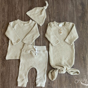 Gender neutral coming home outfit 4 piece bundle. Sandy beige color. Bundle includes a super soft brushed waffle knit long sleeve top, pants, tie hat, and a 0-3M matching waffle knot knotted baby gown with two wooden buttons.