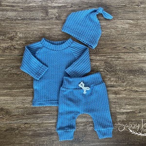 Peut inclure: Un ensemble de v&ecirc;tements pour b&eacute;b&eacute; en tricot gaufr&eacute; bleu avec un t-shirt &agrave; manches longues, un pantalon et un bonnet.
