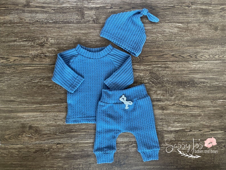 Peut inclure: Un ensemble de v&ecirc;tements pour b&eacute;b&eacute; en tricot gaufr&eacute; bleu avec un t-shirt &agrave; manches longues, un pantalon et un bonnet.