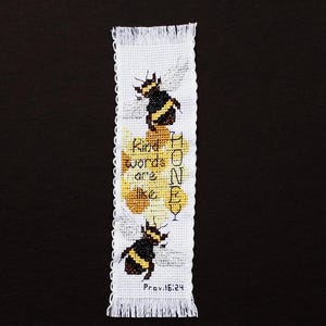 May include: A white cross-stitch bookmark with fringed edges. The design features two bees, honeycombs, and the text "Kind words are like honey" with "Prov 16:24" below. The bees are black and yellow.