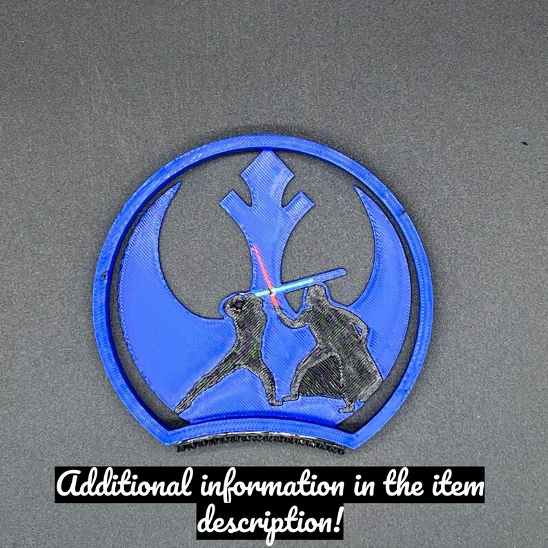 Puede incluir: Un emblema azul y negro impreso en 3D que representa un duelo de sables de luz dentro de un emblema azul. El texto "Additional information in the item description!" est&aacute; en la parte inferior. El dise&ntilde;o est&aacute; sobre un fondo gris oscuro.