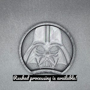 Puede incluir: Un emblema circular gris con la imagen de Darth Vader dentro de un marco circular. La imagen tiene una apariencia impresa en 3D. El texto en la parte inferior dice "Rushed processing is available!"
