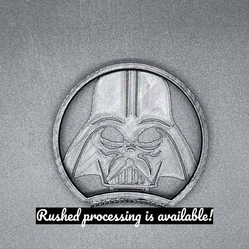 Puede incluir: Un emblema circular gris con la imagen de Darth Vader dentro de un marco circular. La imagen tiene una apariencia impresa en 3D. El texto en la parte inferior dice "Rushed processing is available!"
