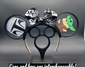 Puede incluir: Orejas de Minnie Mouse negras y blancas con temática de Star Wars con un lazo negro que presenta el logotipo de Star Wars. Las orejas presentan un diseño de Mandalorian y Baby Yoda. Las orejas y el lazo son intercambiables.