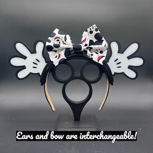 May include: Black headband with Mickey Mouse ears and a bow. The bow is white with black polka dots and Mickey Mouse faces. The ears are black with white gloves on each side. The text at the bottom says "Ears and bow are interchangeable!"