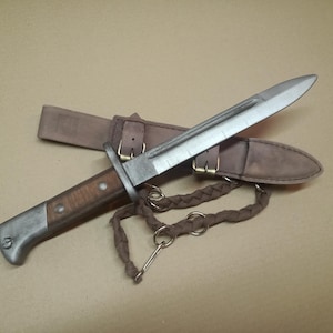 May include: A vintage-style knife with a wooden handle and a silver blade, resting in a brown leather sheath. The knife has a braided cord attached. The sheath has a belt loop and is secured with a buckle. The overall design suggests a historical or collectible item.