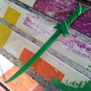 May include: A green wooden sword with a twisted handle lies on a weathered wooden surface painted with stripes of yellow, orange, green, and purple.