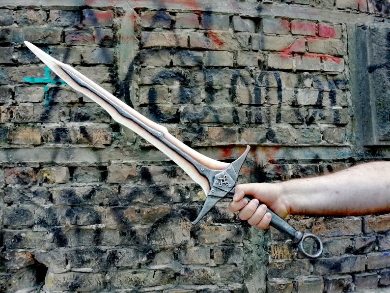 May include: A white and silver sword with a black handle and a ring on the end. The sword has a decorative design on the blade and a cross-shaped design on the pommel.