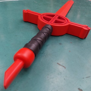 May include: A red wooden sword with a black grip and a cross-shaped design on the blade.