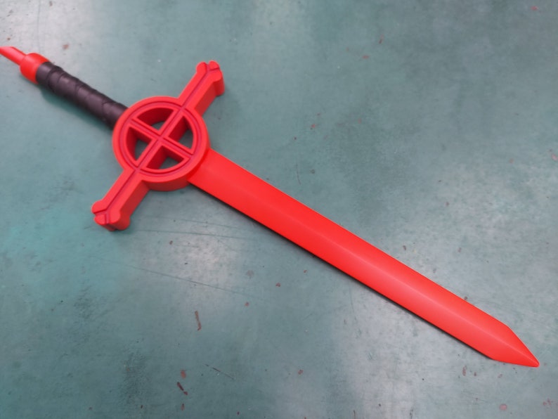 May include: A red plastic sword with a black handle and a circular design on the guard. The design features a cross inside a circle.