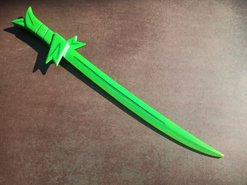May include: A bright green wooden sword with a decorative handle. The sword is lying on a brown surface.