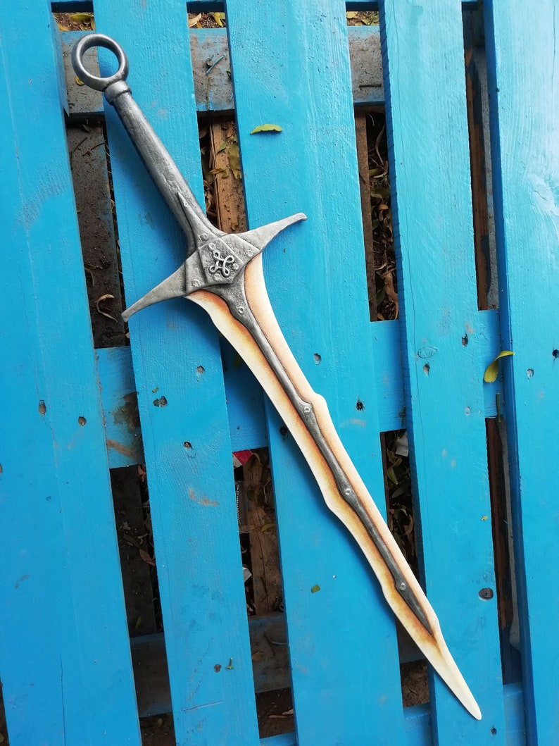 May include: A silver and brown sword with a decorative handle and a pointed blade. The sword is lying on a blue wooden surface.