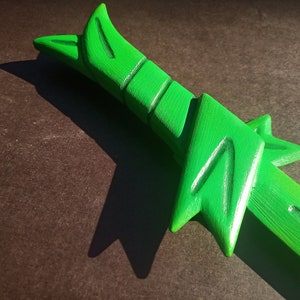 May include: A green plastic toy sword with a detailed design. The sword has a sharp point and a curved handle.