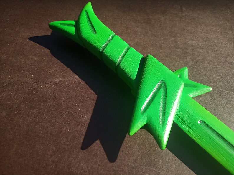 May include: A green plastic toy sword with a detailed design. The sword has a sharp point and a curved handle.