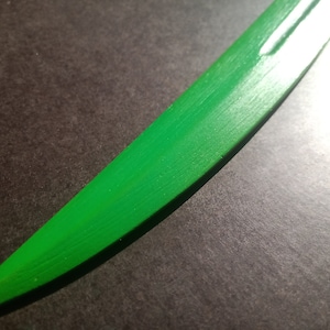 May include: A close-up of a green wooden sword blade. The blade is smooth and has a slight curve.