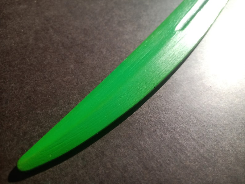 May include: A close-up of a green wooden sword blade. The blade is smooth and has a slight curve.