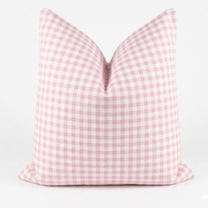 May include: A square decorative pillow with a pink and white gingham pattern. The pillow is a soft pink color and has a classic, checkered design. The pillow is a home decor item.