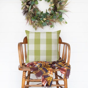 May include: A wooden chair with a green and white checkered pillow and a brown and orange plaid throw blanket.