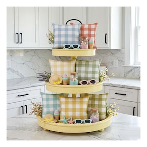 May include: A three-tiered yellow serving tray with decorative pillows, sunglasses, and beach-themed accessories. The pillows feature a gingham pattern in various colors. The tray is decorated with miniature ice cream cones, starfish, and small jars.