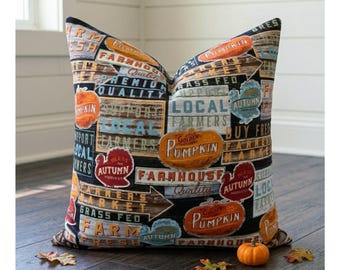 May include: A square throw pillow featuring a black background with a collage of vintage-style signs. The print includes text such as Farm Fresh, Local Farmers, and Pumpkin, alongside illustrations of pumpkins and turkeys in orange, red, and blue.