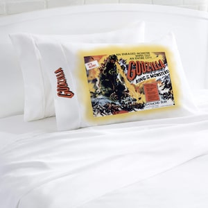 May include: A white pillow with a red "Godzilla" embroidered on it. The pillow has a vintage movie poster printed on it featuring Godzilla, the text "It's Alive!" and "Godzilla King of the Monsters!" and the actor's name "Raymond Burr".