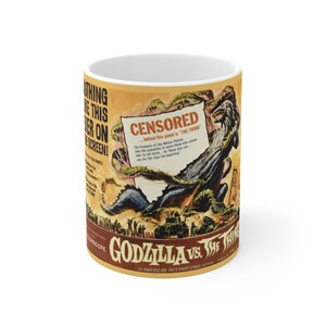 May include: A white ceramic mug with a vintage movie poster design featuring Godzilla and a censored scene. The poster is yellow, brown, and green with the text "GODZILLA VS. THE THING" and "CENSORED" in red.