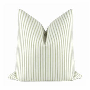 May include: A square throw pillow featuring a vertical striped pattern in light sage green and white. The pillow has a crisp, structured shape with a distinct center fold at the top, creating a symmetrical appearance against a plain white background.