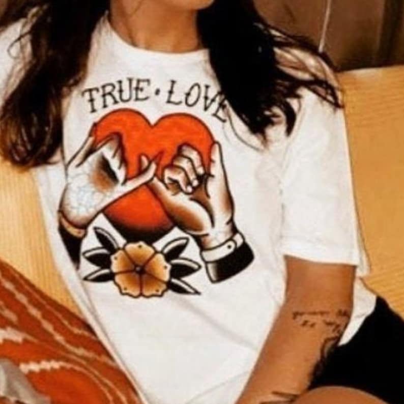 May include: White t-shirt with a red heart and two hands intertwined, a flower below, and the text "TRUE LOVE" above the heart.