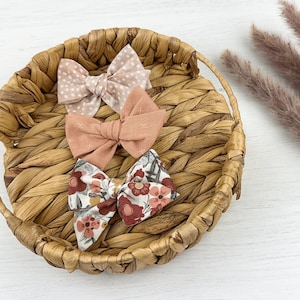 May include: Three fabric hair bows in a woven basket. The bows are in shades of pink and brown with floral and polka dot patterns.