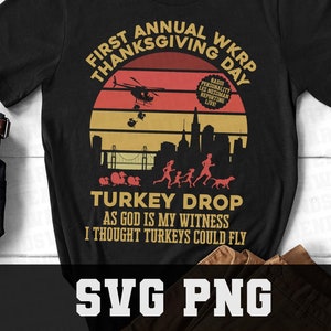 May include: A black t-shirt with a vintage-style graphic design featuring a helicopter dropping turkeys in a city skyline. The text reads "First Annual WKRP Thanksgiving Day" and "Turkey Drop As God is my witness I thought turkeys could fly".