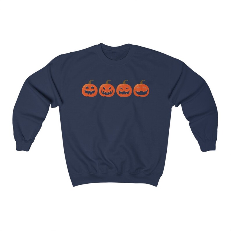 K&ouml;nnte beinhalten: Marineblaues Sweatshirt mit vier orangefarbenen K&uuml;rbisgesichtern mit unterschiedlichen Schnitzereien. Die K&uuml;rbisse sind horizontal angeordnet. Ein lang&auml;rmliges Oberteil f&uuml;r Halloween.