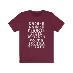 May include: A maroon t-shirt with white text. The text includes the names of Santa's reindeer and alcoholic beverages: Dasher, Dancer, Prancer, Vixen, Whiskey, Vodka, Tequila, and Blitzen. The shirt is a crew neck style.