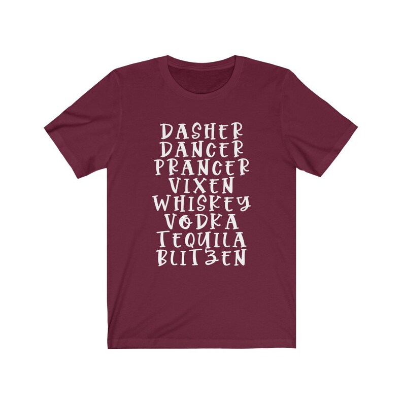 May include: A maroon t-shirt with white text. The text includes the names of Santa's reindeer and alcoholic beverages: Dasher, Dancer, Prancer, Vixen, Whiskey, Vodka, Tequila, and Blitzen. The shirt is a crew neck style.