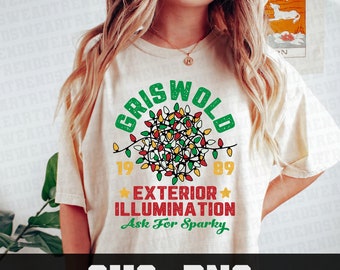 May include: Cream-colored t-shirt with a festive design. The shirt features the word "GRISWOLD" in green above a cluster of colorful Christmas lights. Below the lights are the numbers "1989" and the words "EXTERIOR ILLUMINATION" in red. The phrase "Ask For Sparky" is in green.
