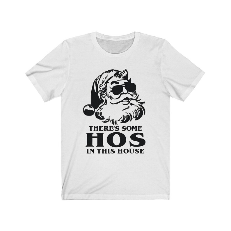 Pu&ograve; includere: T-shirt bianca con grafica nera di Babbo Natale con occhiali da sole. Il testo "THERE'S SOME HOS IN THIS HOUSE" &egrave; stampato sotto. La maglietta ha maniche corte e girocollo, adatta per un look casual.