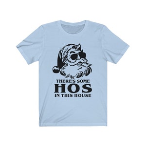 Pu&ograve; includere: T-shirt azzurra con una grafica nera di Babbo Natale con occhiali da sole. Il testo "THERE'S SOME HOS IN THIS HOUSE" &egrave; stampato sotto la grafica di Babbo Natale in un carattere grassetto senza grazie. La maglietta &egrave; realizzata in un materiale morbido.