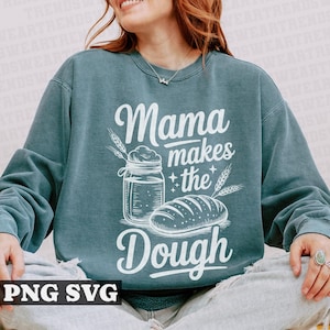 May include: A teal blue sweatshirt with the text "Mama makes the dough" in white. The design includes a jar of dough, a loaf of bread, and wheat stalks.