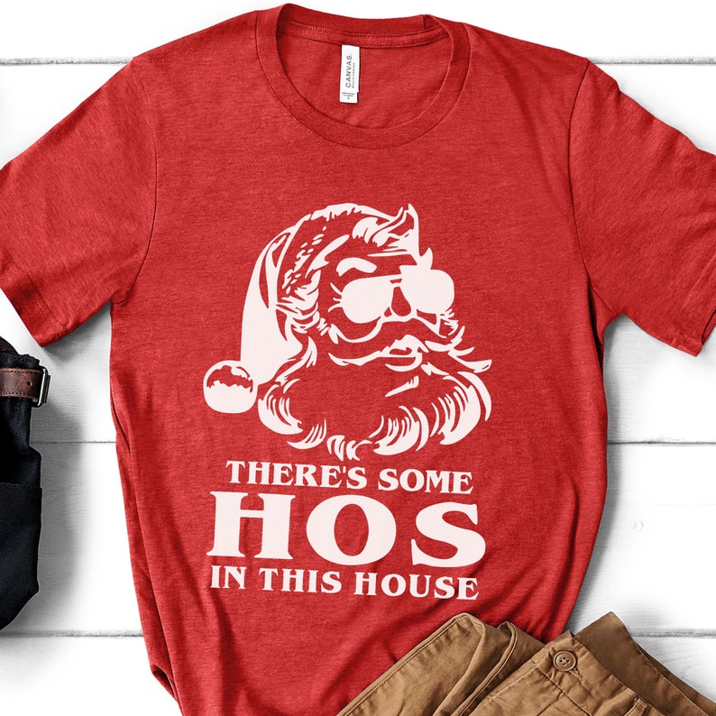 Pu&ograve; includere: T-shirt rosso con grafica bianca di Babbo Natale con occhiali da sole e barba. Il testo "THERE'S SOME HOS IN THIS HOUSE" &egrave; stampato sotto in lettere bianche. La maglietta &egrave; realizzata in materiale morbido.