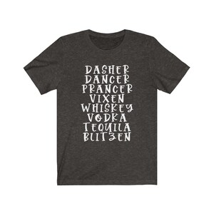May include: Dark grey t-shirt featuring white text with festive words: Dasher, Dancer, Prancer, Vixen, Whiskey, Vodka, Tequila, and Blitzen. The shirt is made of a soft material and has short sleeves.