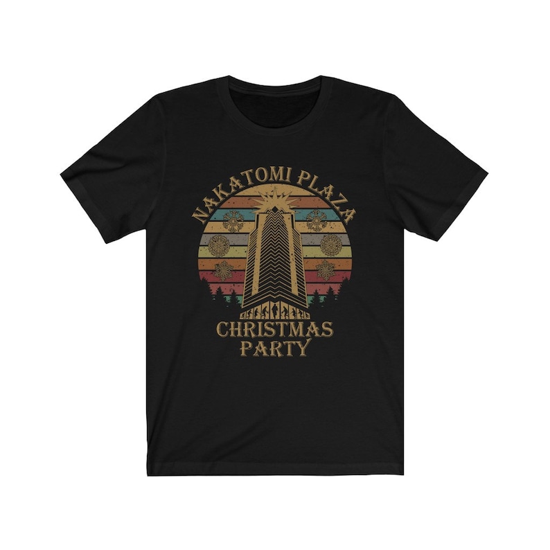 May include: Black t-shirt featuring a retro design with the text "Nakatomi Plaza Christmas Party." The design includes a tall building, a sunset, and decorative elements, evoking a vintage aesthetic.