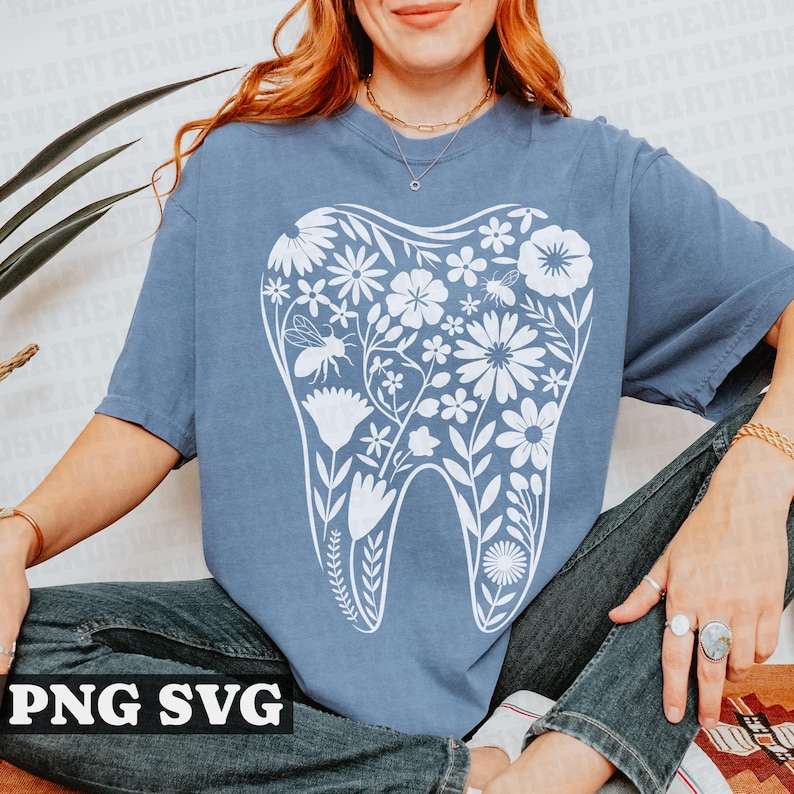 May include: A light blue t-shirt with a white floral design in the shape of a tooth. The design features flowers, leaves, and a bee.