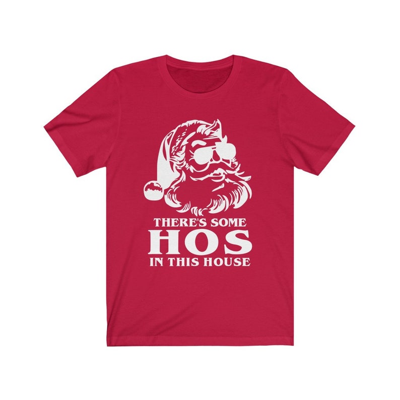 Pu&ograve; includere: T-shirt rossa con grafica bianca di Babbo Natale con occhiali da sole. Il testo "THERE'S SOME HOS IN THIS HOUSE" &egrave; stampato sotto la grafica di Babbo Natale in lettere bianche.