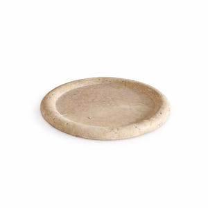 May include: A beige, oval-shaped stone tray with a slightly raised edge. The tray has a natural, textured appearance and is suitable for serving or display. The neutral color complements various decor styles.