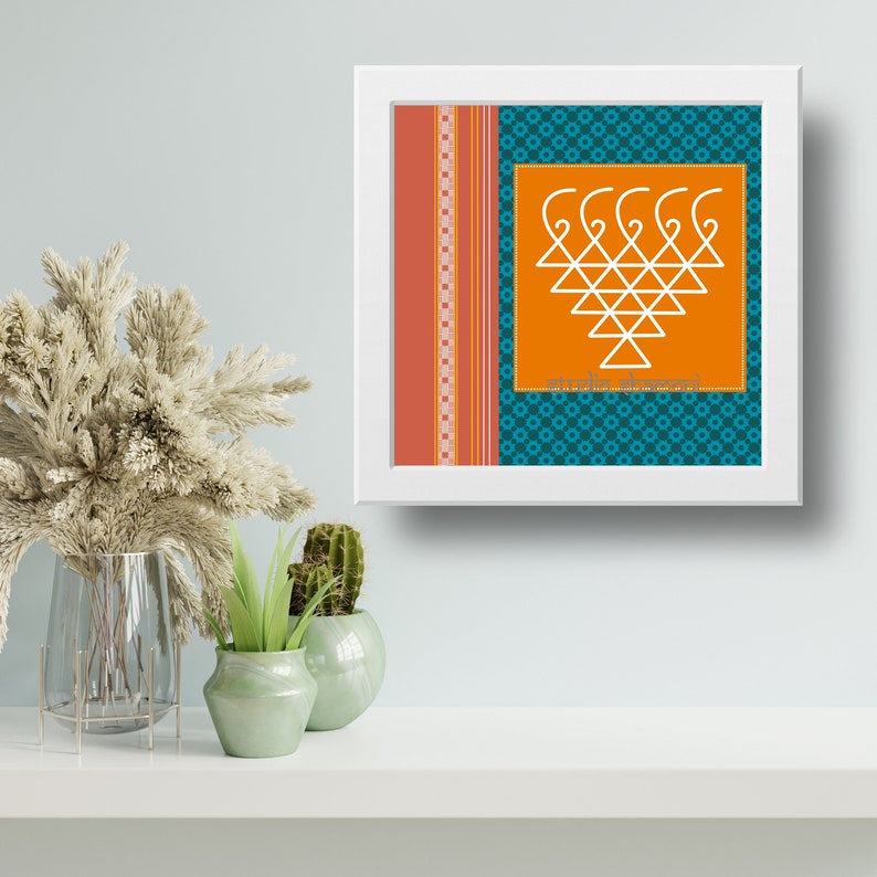 Op de afbeelding: Een ingelijst afdruk met een wit geometrisch ontwerp op een oranje achtergrond. Het ontwerp is omgeven door een turquoise patroonrand. De tekst "Sri Maha Lakshmi" staat onder het ontwerp.