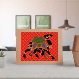 May include: A framed print of a black camel with colorful decorations on a red background with a repeating pattern. The camel is walking to the right.