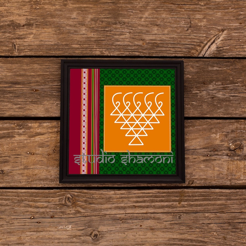 Op de afbeelding: Een ingelijst drukwerk met een wit geometrisch ontwerp op een oranje achtergrond. De lijst is zwart en de passe-partout is groen met een rode en witte gepatroneerde rand. De tekst "Studio Shamoni" is onderaan het drukwerk gedrukt.