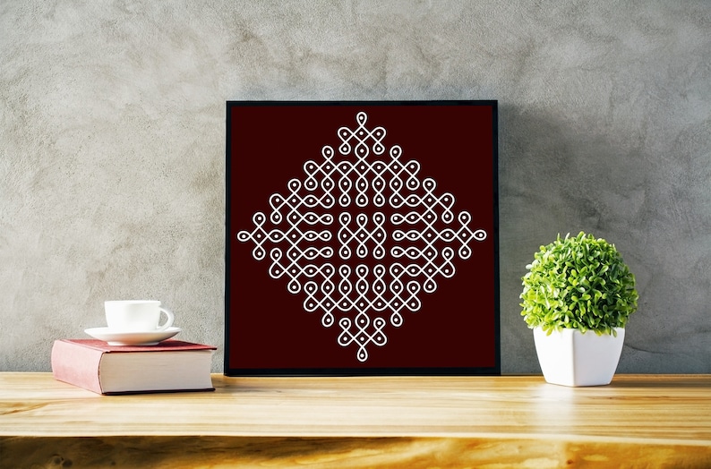May include: A framed print of a white geometric design on a maroon background. The design is a traditional Indian rangoli pattern.