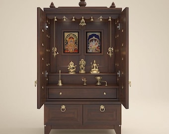 May include: A dark brown wooden home temple cabinet with two open doors, featuring a central shelf holding three brass deity statues, two framed religious images, a brass bell, a small oil lamp, and a brass incense burner, with a lower drawer.